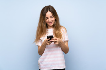 Fototapeta premium Young woman over isolated blue background sending a message with the mobile