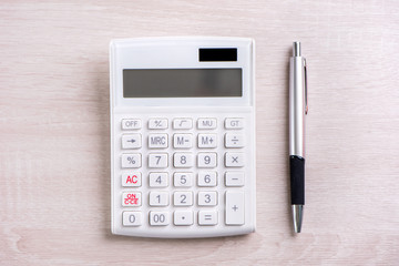 White calculator and pen on bright wooden table, analytics and statistics of financial profit, investment risk concept, copy space, top view flat lay