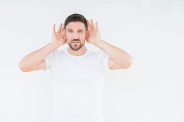 Fototapeta premium Young handsome man wearing casual white t-shirt over isolated background Trying to hear both hands on ear gesture, curious for gossip. Hearing problem, deaf