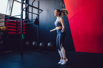 Cheerful woman 20 years old with training equipment enjoying time in sport hall smiling while doing cardio exercises, happy Caucasian female athlete jumping with rope in modern pilates studio