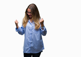 Young beautiful blonde business woman wearing glasses over isolated background very happy and excited doing winner gesture with arms raised, smiling and screaming for success. Celebration concept.