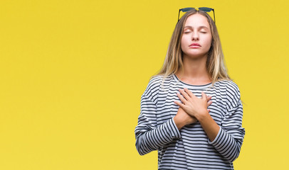 Obraz premium Young beautiful blonde woman wearing sunglasses over isolated background smiling with hands on chest with closed eyes and grateful gesture on face. Health concept.