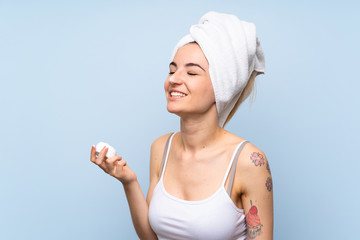 Young woman over isolated blue background with moisturizer