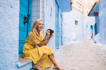 Portrait of happy hipster girl with vintage camera in hands resting in ancient city Morocco...