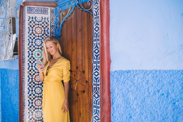 Obraz premium Positive young hipster girl typing text message using 4g wireless for networking and online communication, happy female tourist blogging creating publication about tourism and trip to Chaouen
