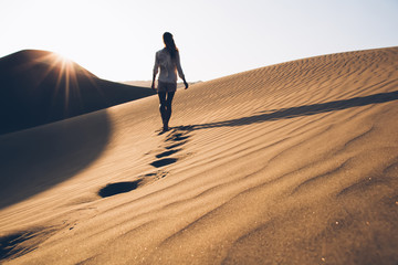 Back view of female wanderer in casual wear exploring wild Sahara desert during summer evening in...