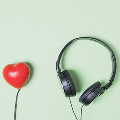 Red heart shape connected to headphone on turquoise background