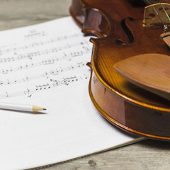 Close-up of pencil and violin on musical note over the wooden table