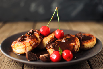 Gourmet breakfast - cottage cheese pancakes, cheese cakes, cottage cheese pancakes with cherries and chocolate in a brown plate. Useful dessert on a wooden table in rustic style. Selective focus.