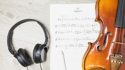 Headphone; pencil; and violin over musical note on wooden background