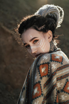 Beautiful young woman with elf ears, dreadlocks and an ethnic poncho, with painted face. Posing against a sandy career or desert.