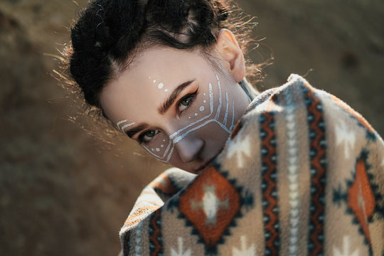 Beautiful young woman with elf ears, dreadlocks and an ethnic poncho, with painted face. Posing against a sandy career or desert.