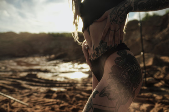 Beautiful sexy woman in black underwear. The body is covered with many tattoos. Dreadlocks on the head . Posing against sandy career and black fabric.