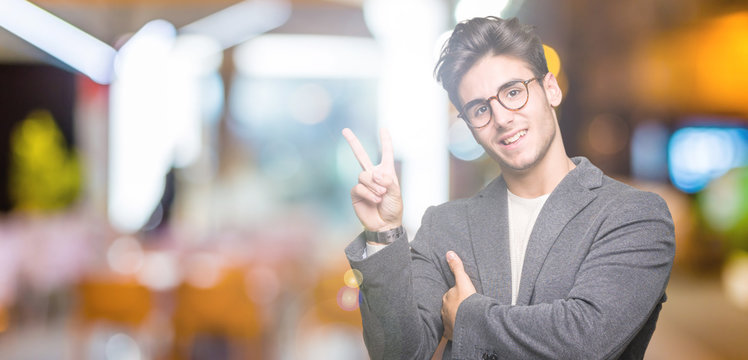 Young business man wearing glasses over isolated background smiling with happy face winking at the camera doing victory sign. Number two.