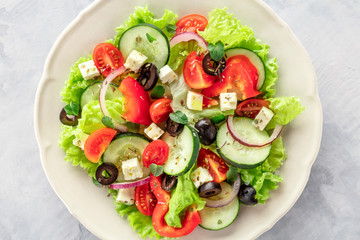 Greek salad closeup. A plate of fresh salad with lettuce, feta cheese, tomatoes, cucumbers, onions and olives, shot from the top