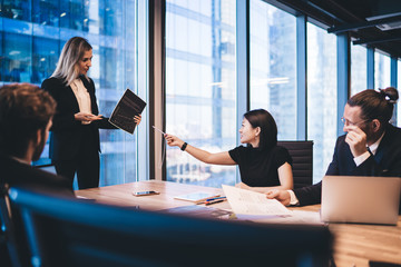Clever male and female coworkers in formal wear collaborating on financial report for company sitting at desktop with modern technology and analyzing data information, concept of brainstorming