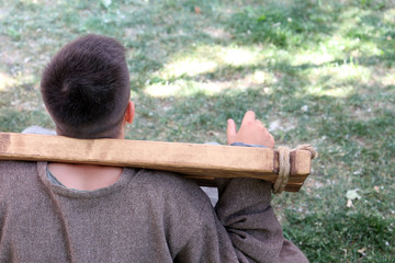 Captive in wooden stocks sitting on a ground. Man with hands tied, slavery and tortures concept