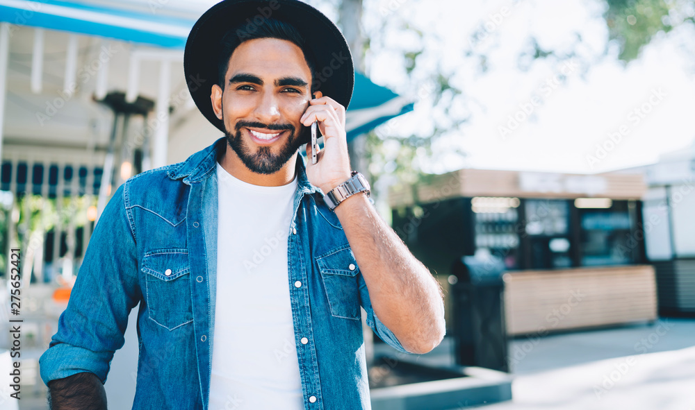 Poster half length portrait of cheerful spanish hipster guy smiling at camera while discussing time of meet
