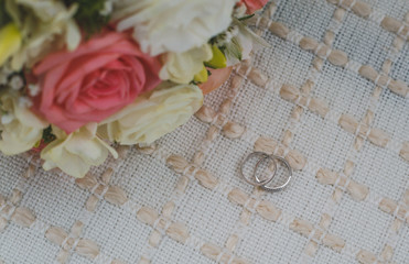 white gold wedding rings lie on a beige rug, a bridal bouquet