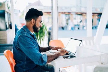 Side view of skilled male online shopper feeling good from spending time for research good deals with discounts connected to wifi internet on modern laptop computer with blank screen area for text