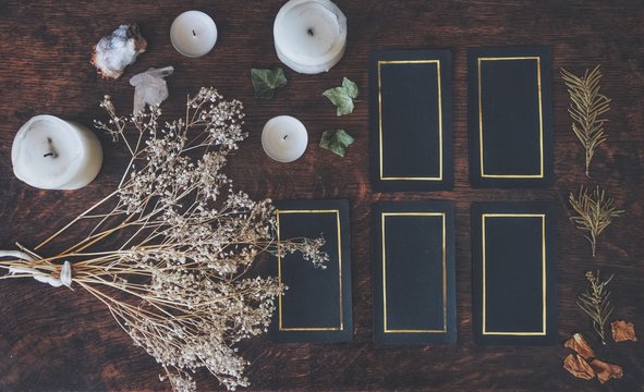 Tarot 5 card spread on a nature display (flat lay) . Hand made tarot cards on a dark wooden table surrounded with dried flowers, herbs and white candles. Black cards with golden shiny rectangular rim