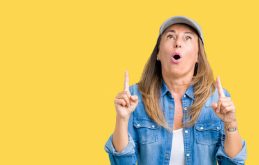 Beautiful middle age woman wearing sport cap over isolated background amazed and surprised looking up and pointing with fingers and raised arms.