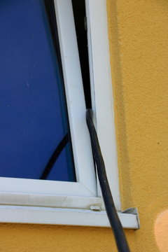 Stromkabel wurde durch ein Fenster geführt. Es besteht die Gefahr des  einklemmen und Kurzschluss. Stock-Foto | Adobe Stock