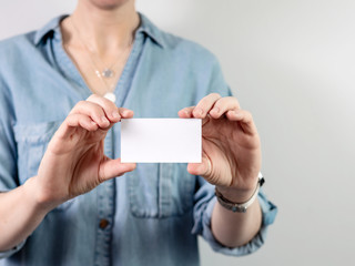 Obraz premium Female hands hold blank white card mockup. Plain call-card mock up template holding woman arm. Caucasian woman in casual blue denim shirt with business card display front. Check offset card design
