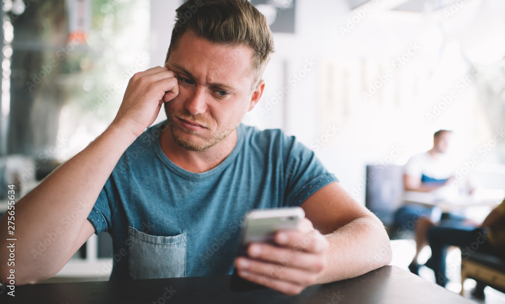 Poster puzzled male blogger feeling tired from online messaging with followers from own website using smart