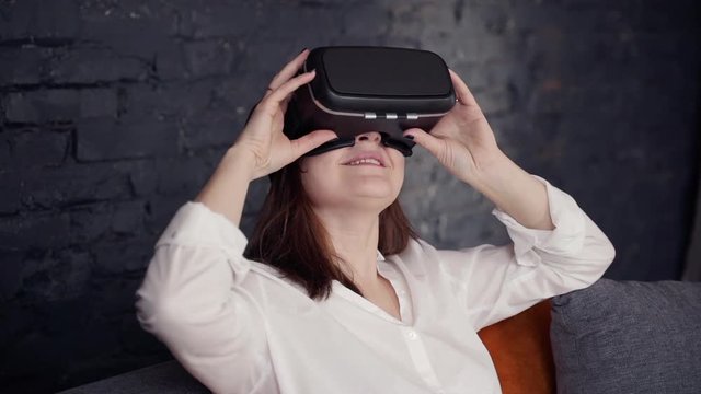 Attractive woman in virtual reality glasses sitting on sofa