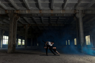 A young girl and boy perform acrobatic moves, are in the premises of the old factory, the composition, blue smoke around them, acro