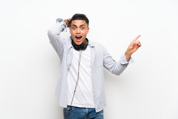 Naklejka premium Young man over isolated white wall with earphones surprised and pointing finger to the side