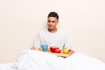 Young man having breakfast in bed standing and looking to the side