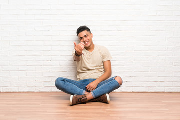Young man sitting on the floor inviting to come