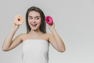 Beautiful young girl in white towel looking aside. She holds flowers in her hands.