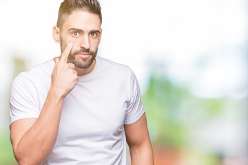 Handsome man wearing white t-shirt over outdoors background Pointing to the eye watching you gesture, suspicious expression