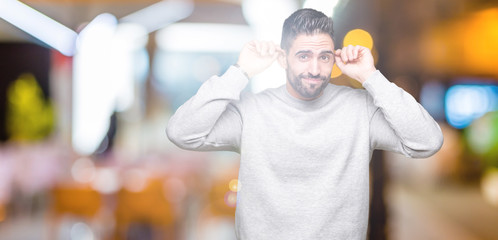 Young handsome man wearing sweatshirt over isolated background Smiling pulling ears with fingers, funny gesture. Audition problem