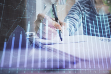 Financial forex graph drawn over hands taking notes background. Concept of research. Double exposure