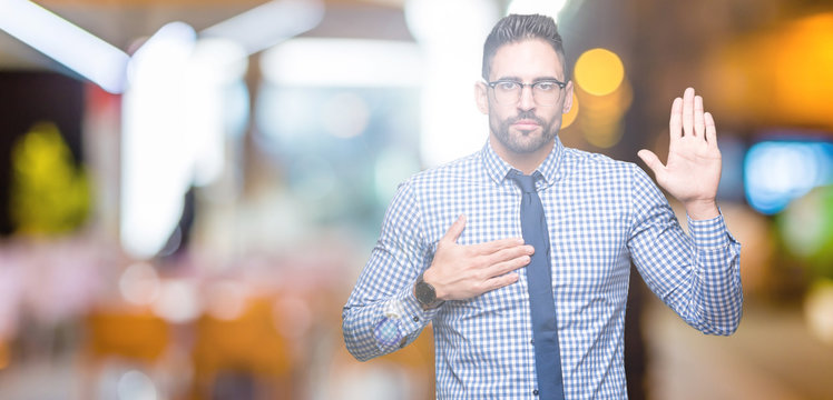 Young business man wearing glasses over isolated background Swearing with hand on chest and open palm, making a loyalty promise oath