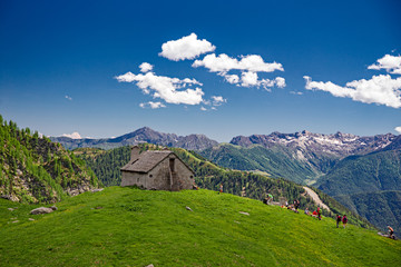 Some hikers near a panoramic mountain pasture in the Alps of Piedmont, Italy.