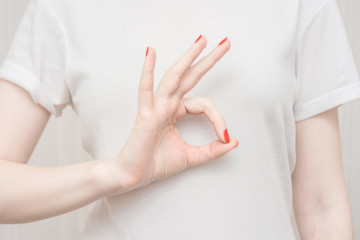 Woman in white polo shirt showing okay gesture, holding a  white t-shirt, close up