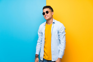 Young man over isolated colorful background with sunglasses