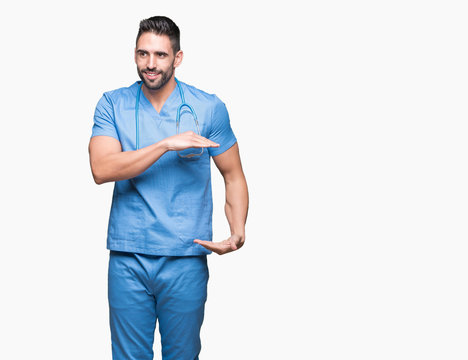 Handsome young doctor surgeon man over isolated background gesturing with hands showing big and large size sign, measure symbol. Smiling looking at the camera. Measuring concept.