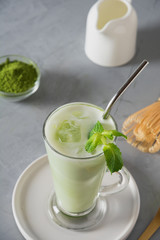 Green cold matcha tea in latte glass with ice cube and milk on grey table. Close up. View from above.