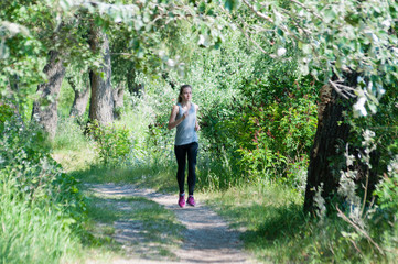 Obraz premium Beautiful, athletic, slim woman with headphones running through the park in the summer sunny morning. Morning jogging and sports