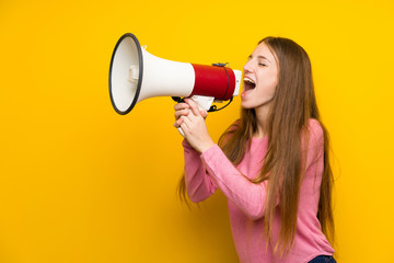 Young woman with long hair over isolated yellow wall shouting through a megaphone