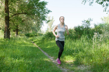 Beautiful, athletic, slender woman with headphones and sports suit runs through the park, summer, sunny morning. Morning jogging and sports