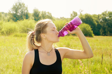 Young woman with a sporty figure, body, slim, after a workout drinks water from bottle