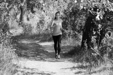 Athletic, beautiful girl runs in the park and listens to music, sunny summer morning, bw