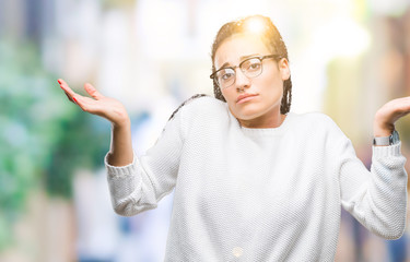 Young braided hair african american girl wearing glasses and sweater over isolated background clueless and confused expression with arms and hands raised. Doubt concept.